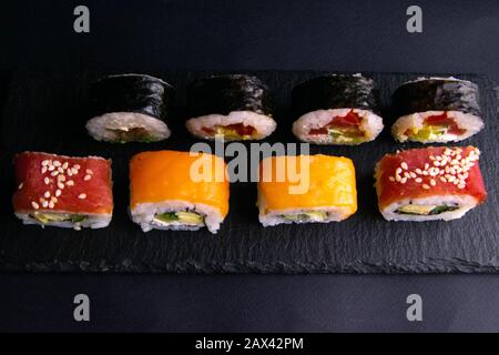 Verschiedene Brötchenarten stehen auf einem schwarzen Granitbrett für Sushi auf schwarzem Grund Stockfoto