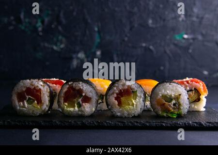 Verschiedene Brötchenarten stehen auf einem schwarzen Granitbrett für Sushi auf schwarzem Grund Stockfoto