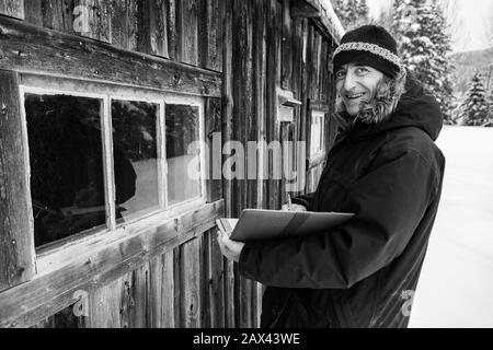 Hausinspektor mittleren Alters, der bei einer Inspektion Notizen auf einem Notizbuch machte. Lächelnder kaukasischer Mann mit Winterkleidung im Freien im Schnee, schwarz und weiß Stockfoto