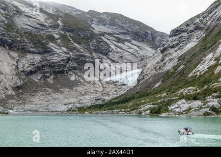 Norwegen Berge Landschaft Blick in der Nähe des Sees mit azurblauem Wasser, Boot, Felsen, Gletscher, Schnee. Bewölkte Tages-Tracking-Reise nach Nigardsbreen in Jostedalsbree Stockfoto