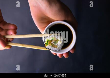 Stöcke rasieren die Rolle von Mohn über einen Teller Sojasoße, eine Platte in einer schönen weiblichen Hand über einem schwarzen Hintergrund Stockfoto
