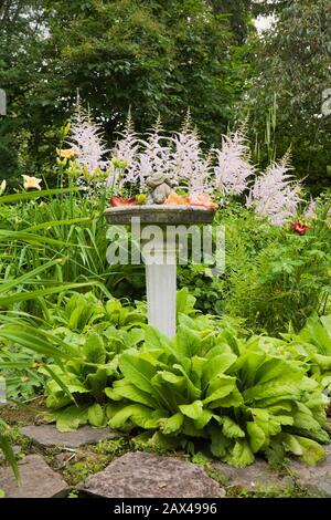 Steinweg und Grenze mit Vogelbad, rosa Astilbe 'Venus', gelb, orange und rot Hemerocallis - Daylilienblumen in privaten Garten Stockfoto