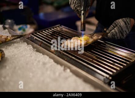 Auf einem Nachtmarkt in Bangkok, Thailand bereitet der Koch frische Meeresfrüchte mit einem bunsenbrenner zu Stockfoto