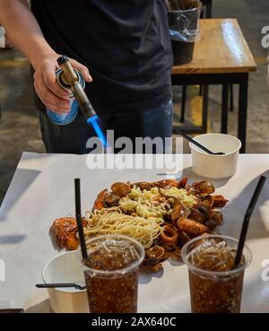 Der Koch bereitet auf einem Nachtmarkt in Bangkok, Thailand, Straßennahrung mit einem bunsenbrenner direkt am Tisch zu. Stockfoto