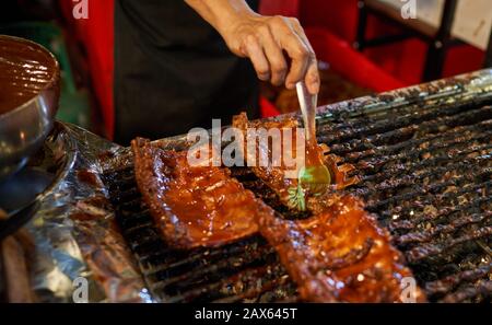 Der Küchenchef bereitet auf einem Nachtmarkt in Bangkok, Thailand, Ersatzrippen auf einem Grill zu. Stockfoto