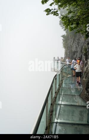 Zhangjiajie, China - August 2019: Touristen, die auf einem schmalen Glasweg im Tianmenshan Naturpark laufen Stockfoto