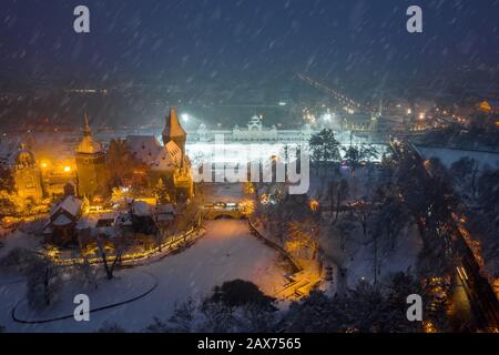 Budapest, Ungarn - Blick Auf die wunderschöne verschneite Burg Vajdahunyad im Stadtpark zu blauer Stunde mit Weihnachtsmarkt, Eisbahn und Heldenplatz Stockfoto