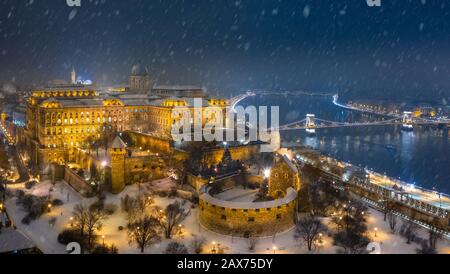 Budapest, Ungarn - Luftbild des beleuchteten Königspalasts der Buda-Burg in einer Winternacht mit schwerem Schnäppen, Szechenyi-Kettenbrücke und Matthias Chur Stockfoto