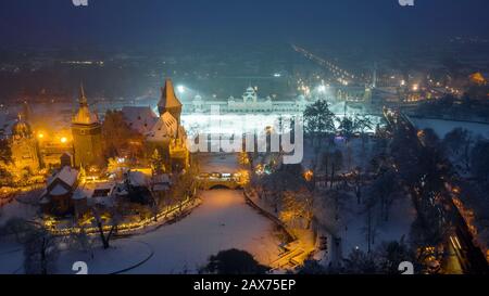 Budapest, Ungarn - Blick Auf die wunderschöne verschneite Burg Vajdahunyad im Stadtpark zu blauer Stunde mit Weihnachtsmarkt, Eisbahn und Heldenplatz Stockfoto