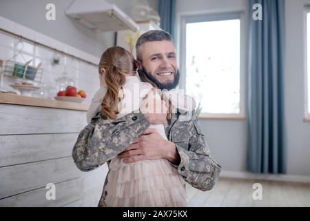 Dienstmann Papa, der nach Hause zurückkehrt und die kleine Tochter umarmt. Stockfoto