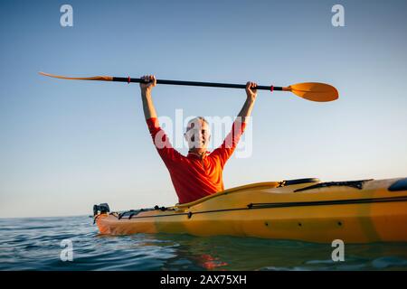 Lächelnder älterer Mann im Kajak hält Paddel hoch Stockfoto