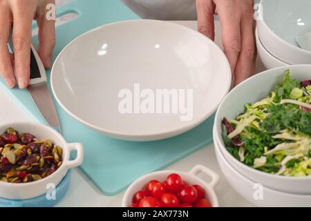 Frau bereitet Gemüsesalat zu. Nahaufnahme von frischem biologischem Gemüse, Kohlmischung, Tomaten, getrockneten Preiselbeeren und Kürbissamen auf einem Küchentisch Stockfoto