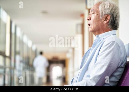 Asiatischer alter Mann, der auf dem Flur des Krankenhauses sitzt, sieht traurig und depressiv aus Stockfoto