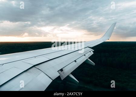 Flügel eines Flugzeuges auf Wolken, Blick vom Flugzeugfenster bei Sonnenuntergang. Stockfoto