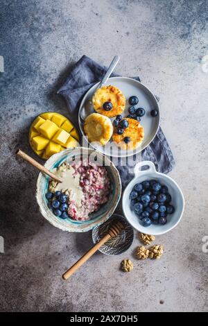 Frühstücksshintergrund. Haferbrei, Käsekuchen mit Beeren und Früchten auf dunklem Hintergrund. Stockfoto