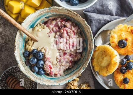 Frühstücksshintergrund. Haferbrei, Käsekuchen mit Beeren und Früchten auf dunklem Hintergrund. Stockfoto