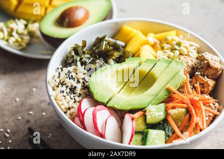 Vegane Poke-Schüssel mit Avocado, Tofu, Reis, Algen, Karotten und Mangos. Veganes Lebensmittelkonzept. Stockfoto