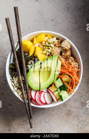 Vegane Poke-Schüssel mit Avocado, Tofu, Reis, Algen, Karotten und Mangos. Veganes Lebensmittelkonzept. Stockfoto