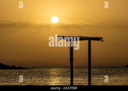 Konzentrieren Sie sich auf die runde Umgebung Sonne. Verschwommene Duschen Silhouette am Strand bei Sonnenuntergang vor dem goldenen Ionischen Meer Wasser in der Nähe des Strandes. Abenddämmerung aus Ksamil, Albanien, Frühlingslandschaften. Stockfoto