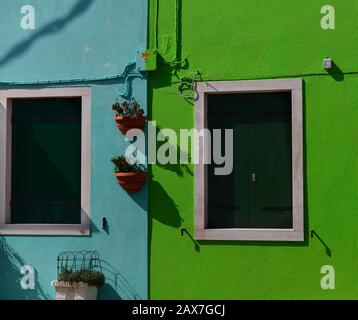 Zwei bunte Fassaden in Blau und Grün mit Fenstern und Blumentöpfen. Burano, Italien Stockfoto