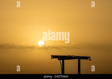 Konzentrieren Sie sich auf die runde Umgebung Sonne. Verschwommene Duschen Silhouette am Strand bei Sonnenuntergang vor dem goldenen Ionischen Meer Wasser in der Nähe des Strandes. Abenddämmerung aus Ksamil, Albanien, Frühlingslandschaften. Stockfoto