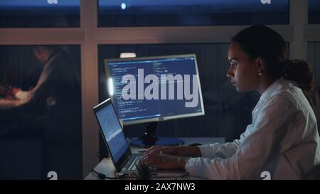 Seitenansicht der afroamerikanischen Ingenieurin, die im Elektroniklabor am Computer arbeitet. Entwicklung von Software und Hardware. Sie trägt einen Labormantel Stockfoto