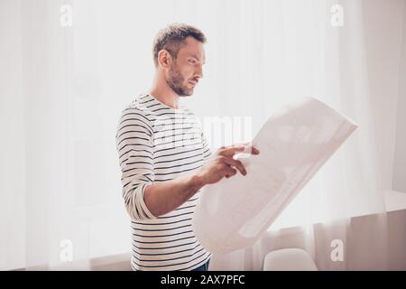 Konzentrierter Architekt, der Blaupause hält und sich das Schema seines Projekts ansieht Stockfoto