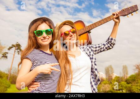 Zwei hübsche Mädchen in Brille und Hüten, die mit Gitarre laufen Stockfoto