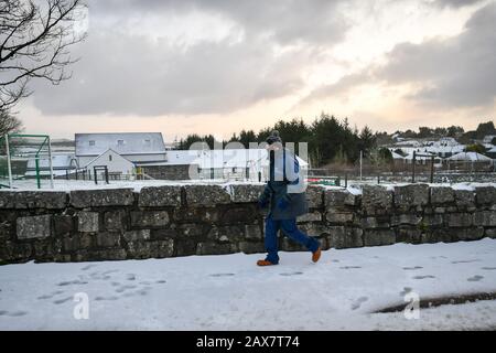 Ein Mann spaziert auf schneebedeckten Fußwegen in Princetown auf der Spitze von Dartmoor, Devon, wo auf hohem Boden Schnee gefallen ist. Stockfoto