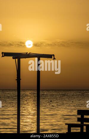 Konzentrieren Sie sich auf die runde Umgebung Sonne. Verschwommene Duschen Silhouette am Strand bei Sonnenuntergang vor dem goldenen Ionischen Meer Wasser in der Nähe des Strandes. Abenddämmerung aus Ksamil, Albanien, Frühlingslandschaften. Stockfoto