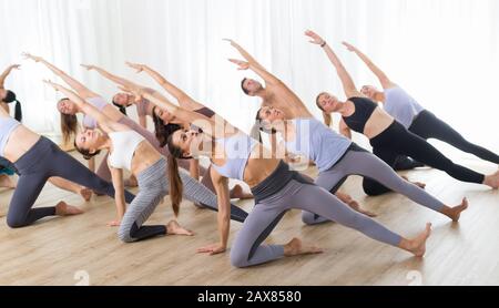 Gruppe von jungen sportlich attraktive Leute im Yoga Studio, Yoga Unterricht mit Kursleiter, Stretching auf Fußboden im Trikonosana, Dreieck yoga Pose Stockfoto
