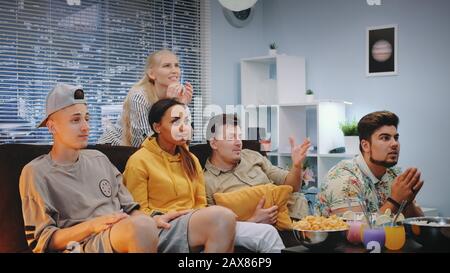 Fröhliche Zuschauer, die Sport im Fernsehen verfolgen und Popcorn verschütten, wenn das Team punktet. Sie sind äußerst glücklich, schreien, springen und heben geklungene Fäuste auf. Stockfoto