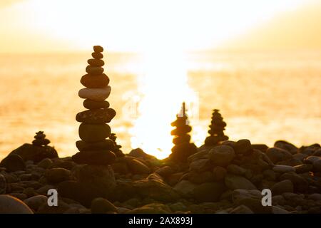 Balancierte Steinpyramide am Ufer des Ozeans im Morgengrauen. Der Turm mit Meeresschälchen steht für Stabilität, Zen, Harmonie und Gleichgewicht. Stockfoto