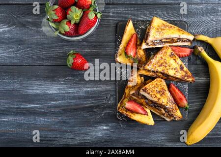 Süße französische Toasts mit Bananen, Schokolade, Erdbeeren auf Holzgrund. Leckeres Frühstück. Draufsicht Stockfoto