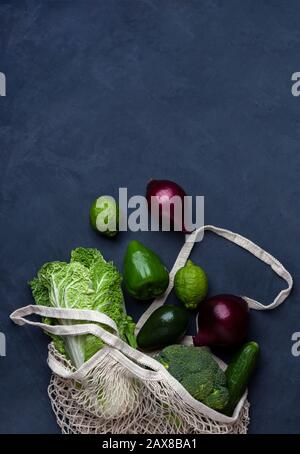 Grünes Gemüse und Obst in einer wiederverwendbaren Netztasche auf blauem Hintergrund. Null-Abfall-Konzept mit Kopierraum. Stockfoto