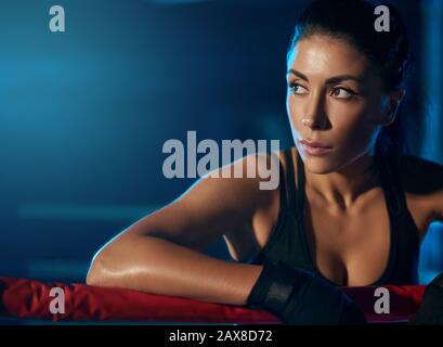 Nahaufnahme von jungen Profi-Kickboxern mit starkem Gesicht, die trendige Sportkleidung und Binden an Händen tragen. Kämpfer, die nach dem Training ruhen und sich an Seil lehnen. Konzept Sport, Boxen. Stockfoto