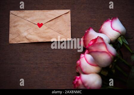 Rosa Rosen Blumenstrauß & Liebesbrief auf altem Holzhintergrund mit Kopierraum. Konzept für Valentinstag, Jahrestag, Grußkarte, Pamphlet, Einband, Stockfoto