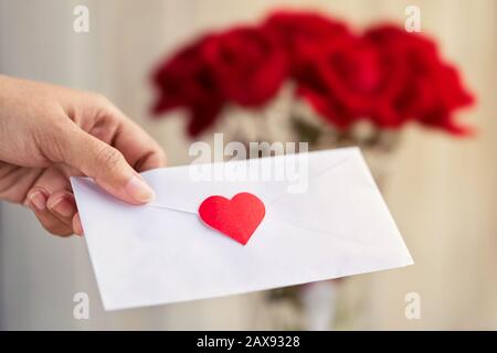 Frau, die Liebesbrief und eine Vase voller roter Rosen im Hintergrund mit Kopierraum verschwimmen. Konzept für die Liebe der Paare, valentinstag Stockfoto