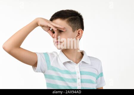 Kleiner Junge im gestreiften T-Shirt, der Geste tut, riecht schlecht auf weißem Hintergrund. Gesichtsausdruck. Kind bedeckt Nase mit der Hand, riecht etwas schreckliches Stockfoto