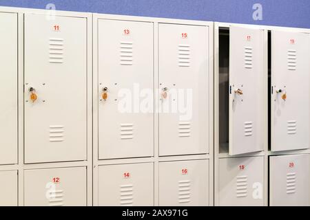Eine Reihe graumetallener Schulschließfächer mit Schlüsseln in den Türen. Stauraum im Flur der Bildungseinrichtung Stockfoto