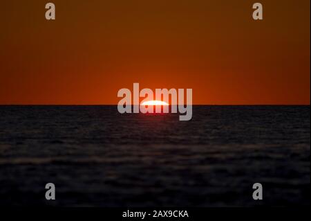 Der Beginn eines Sonnenaufgangs über dem Ozean mit der Sonne, die gerade über den ruhigen Wasserhorizont hinausgeht. Stockfoto