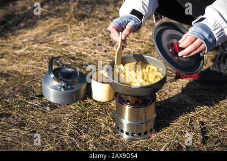 Nahaufnahme der Hände der Wanderer, die Pasta auf einem tragbaren Holzofen kochen. Pasta in den Bergen kochen Stockfoto