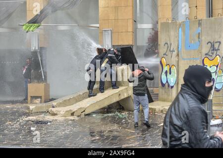 Stadtzentrum Von Beirut, Libanon. Februar 2020. Demonstranten schützen sich hinter Baustellenaushürungen als Polizei-Löschwasserkanon bei ihnen. Die Menschen versammelten sich, um gegen Barrieren zu protestieren, die verhindern, dass sie am Tag eines Vertrauensvotums in das neue Kabinett, das von Interimschef Hassan Diab vorgeschlagen wurde, das parlament erreichen. Credit: Elizabeth Fitt/Alamy Live News Stockfoto