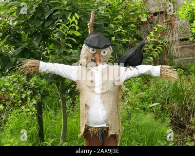 Scarecrow aus Heu, mit Burlapweste, Maisnase, Beret und Krähe auf der Schulter, die in einem Garten stehen Stockfoto