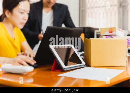 Geschäftspaar, das zu Hause an einem Laptop arbeitet, mit Paket auf dem Tisch, SME Start up Stockfoto