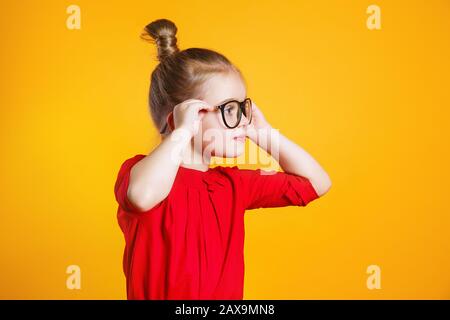 Lustige Kindermädchen in Brille, die auf gelbem Hintergrund wegschaut Stockfoto