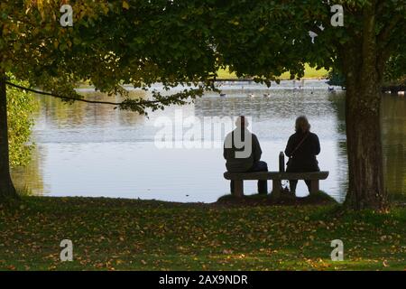 Mann und Frau sitzen mit einem Fläschchen auf dem Sitz am See. Silhouette. Stockfoto