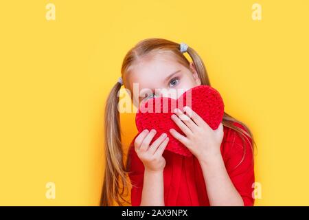 Foto des hübschen kleinen Mädchens hält rotes Papierherz auf gelbem Hintergrund Stockfoto