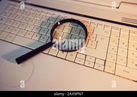 Nahaufnahme einer Lupe auf einer alten Laptop-Tastatur. Computer-Suchmaschine. Durchsuchen des Netzwerks nach Antworten auf jede Frage. Nützliche Informationen finden Stockfoto