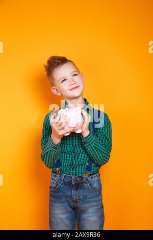 Kleiner Junge, der eine Schweinebank in seinen Händen auf gelbem Hintergrund hält Stockfoto